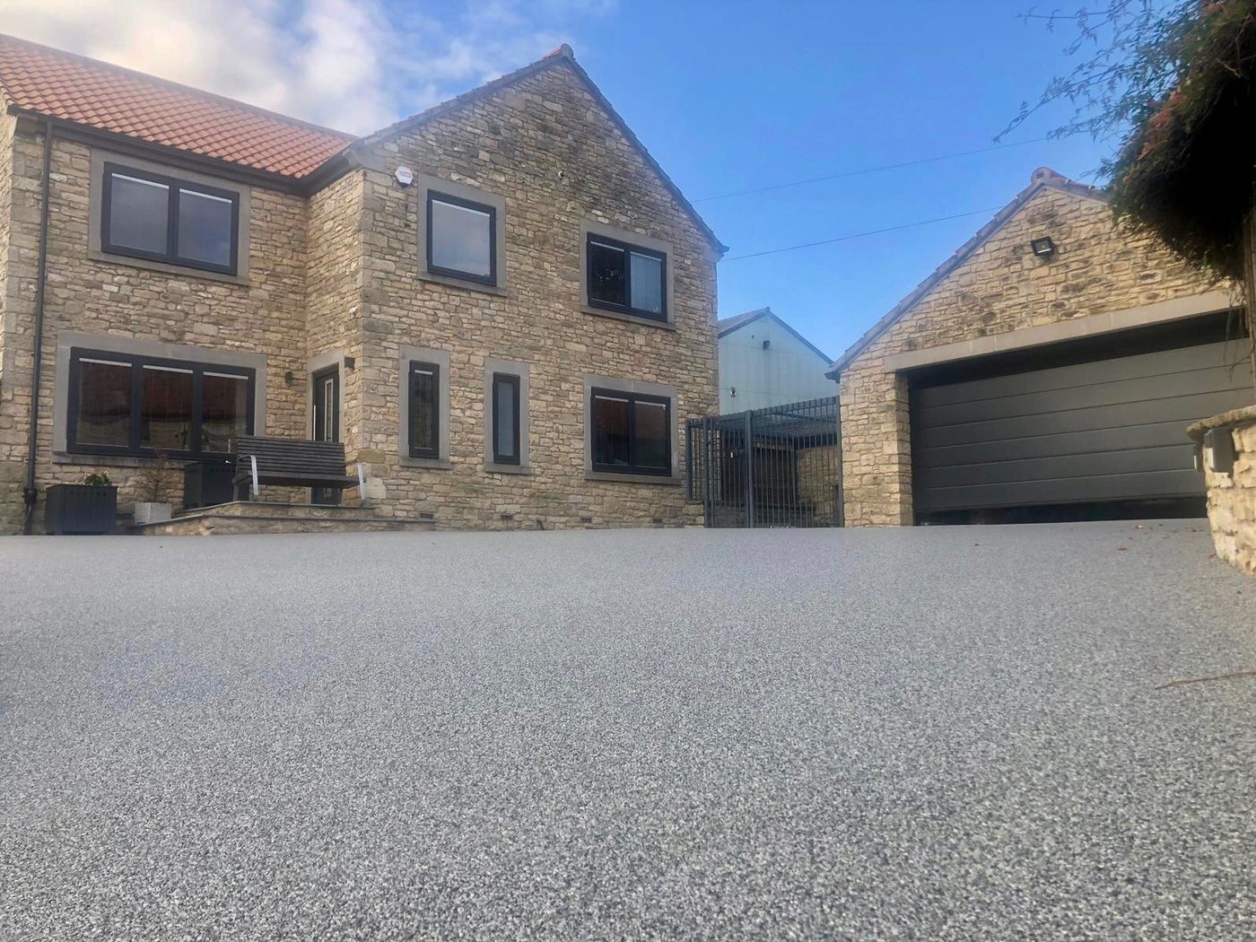 Newly installed silver resin bound driveway in front of a UK stone house with double garage