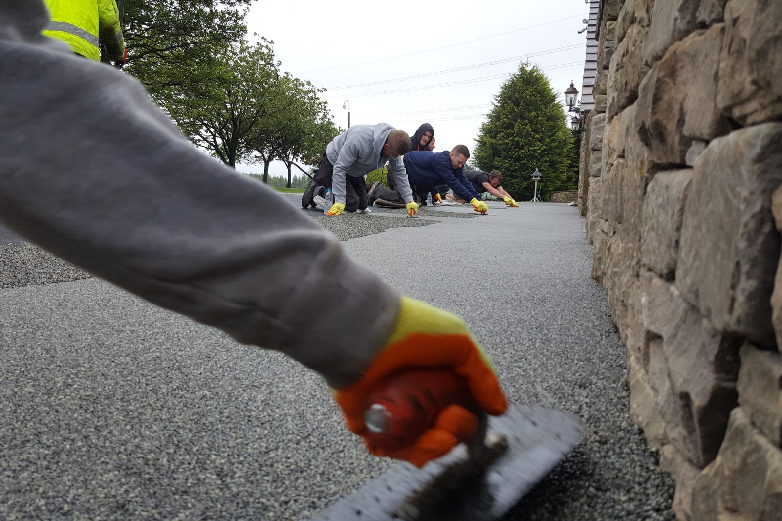 Five-person installation crew laying a grey resin-bound driveway
