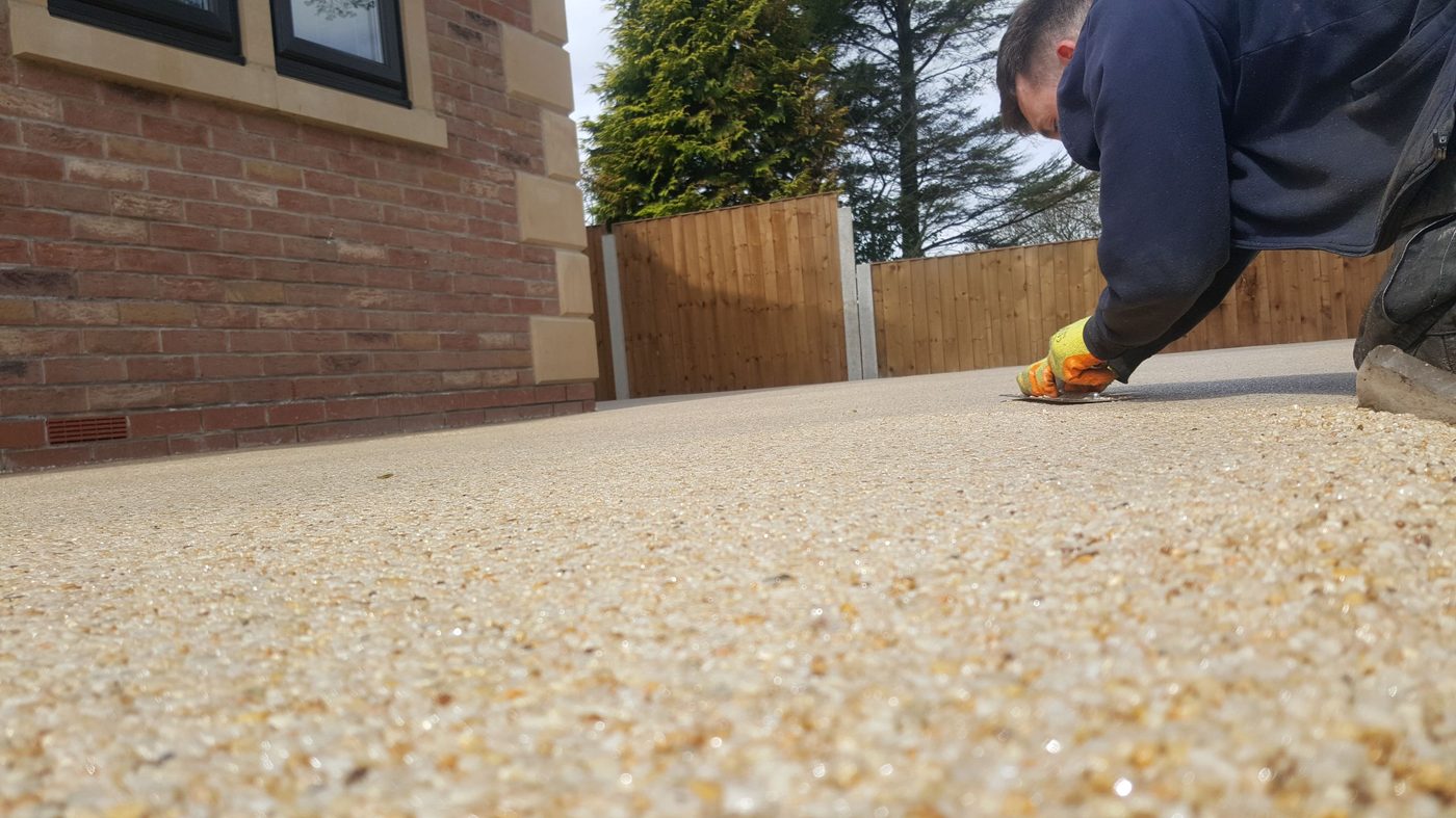 Resin driveway installer kneeling and troweling freshly laid golden resin bound gravel